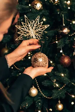 Femme accroche une boule de Noël à son sapin.