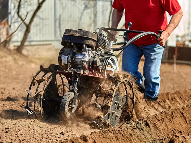 Homme retourne la terre au motoculteur.